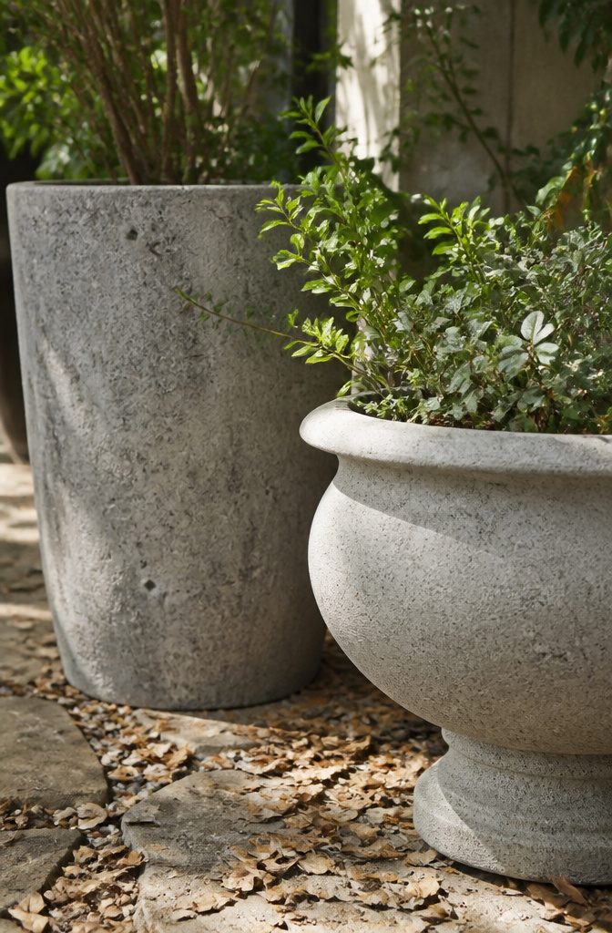 Close-up of poured concrete and cast stone planters against garden foliage.